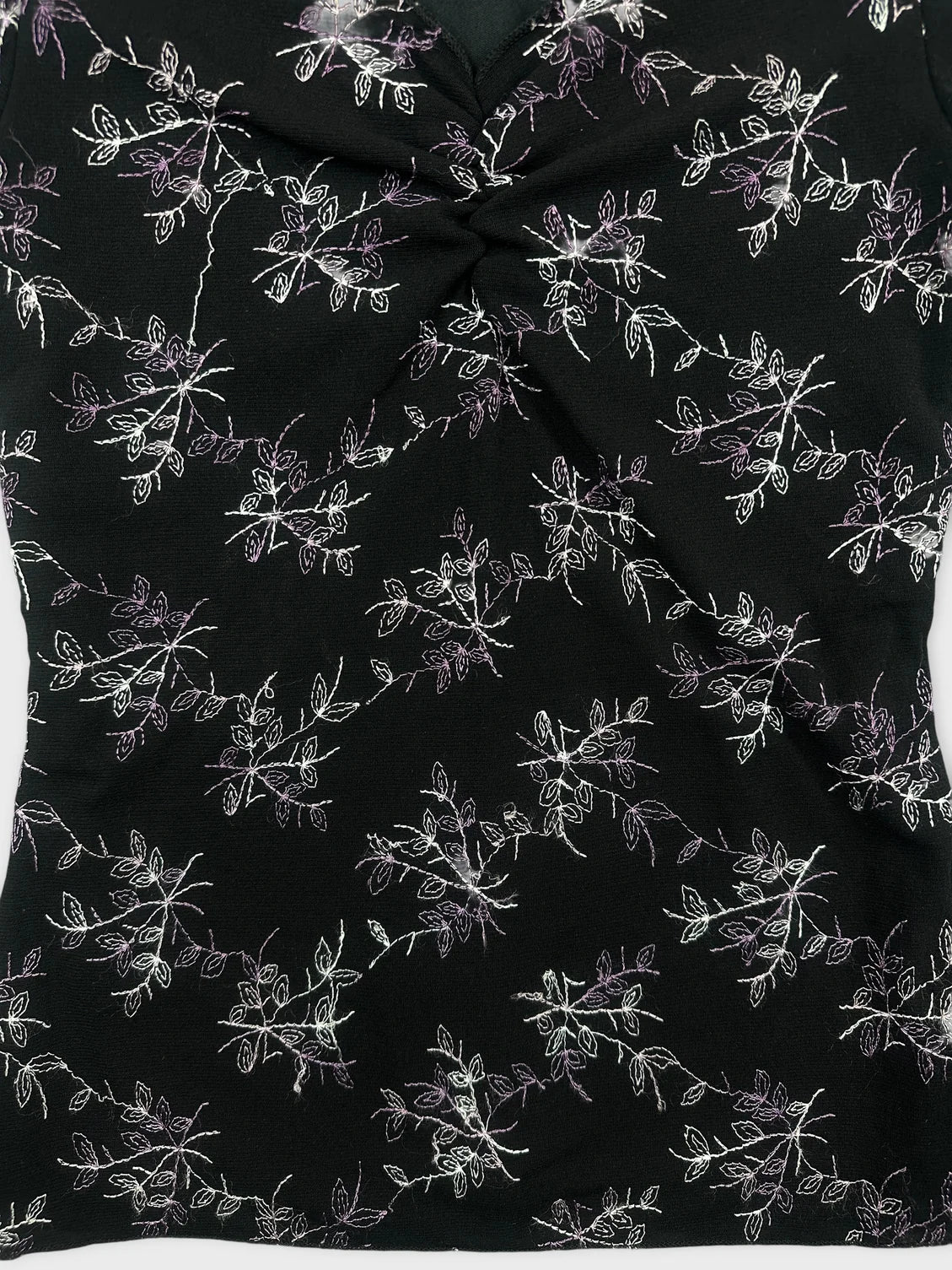 Detail view of a black floral embroidered top with a twisted front detail.