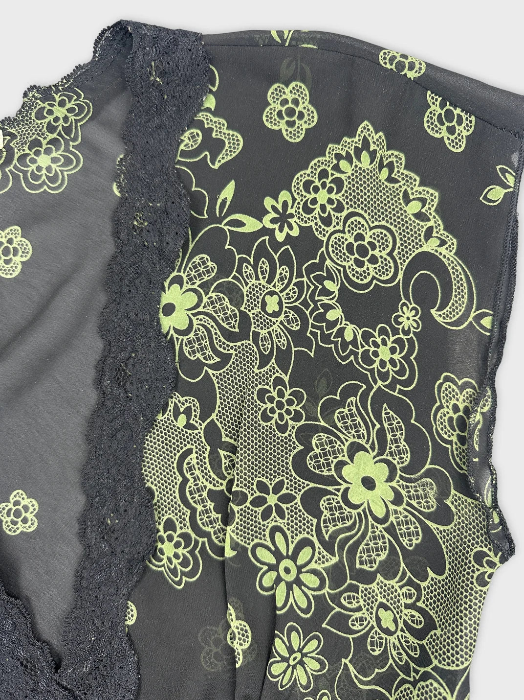 Detail view of a black top with green floral lace trim.