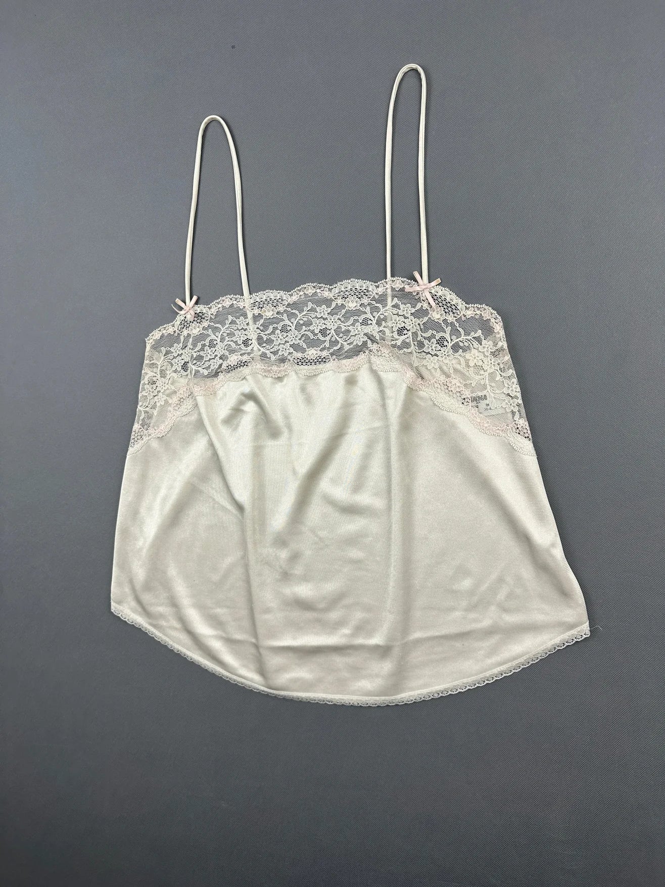 Detail view of a cream camisole top with lace trim and spaghetti straps.