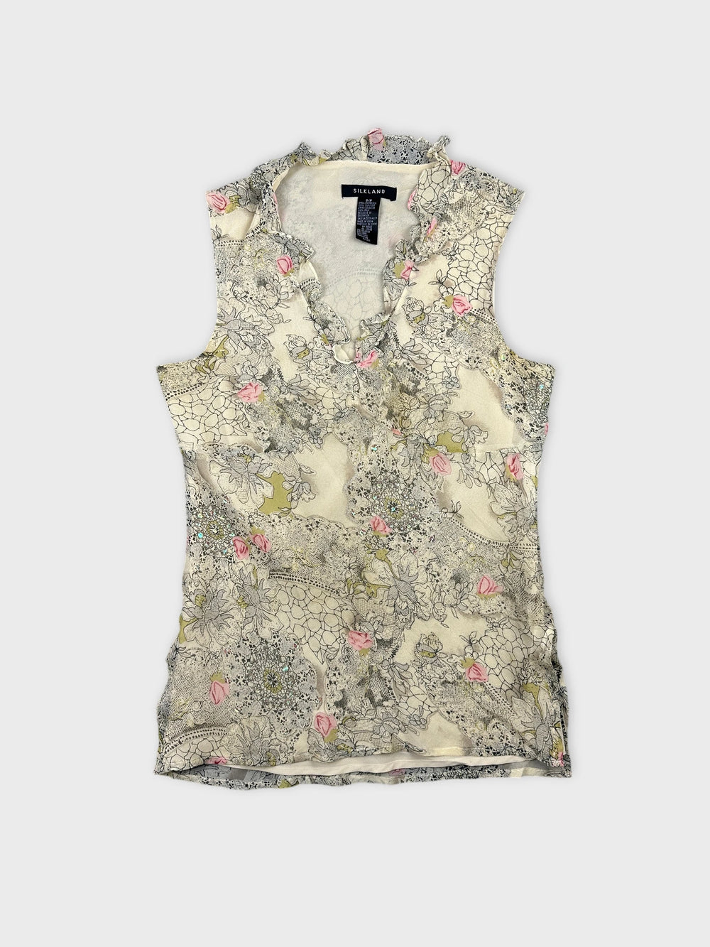 Front view of a sleeveless floral top in cream with ruffled edges.