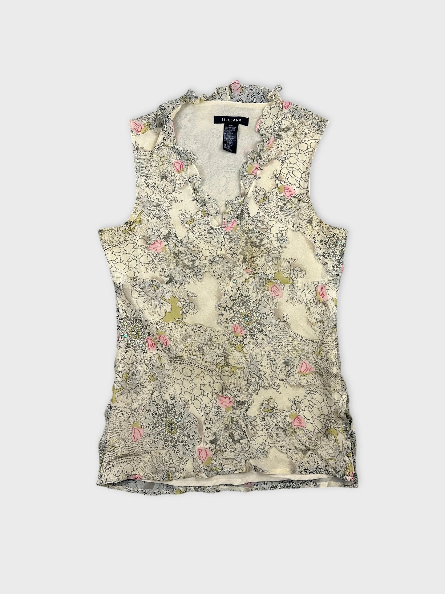 Front view of a sleeveless floral top in cream with ruffled edges.