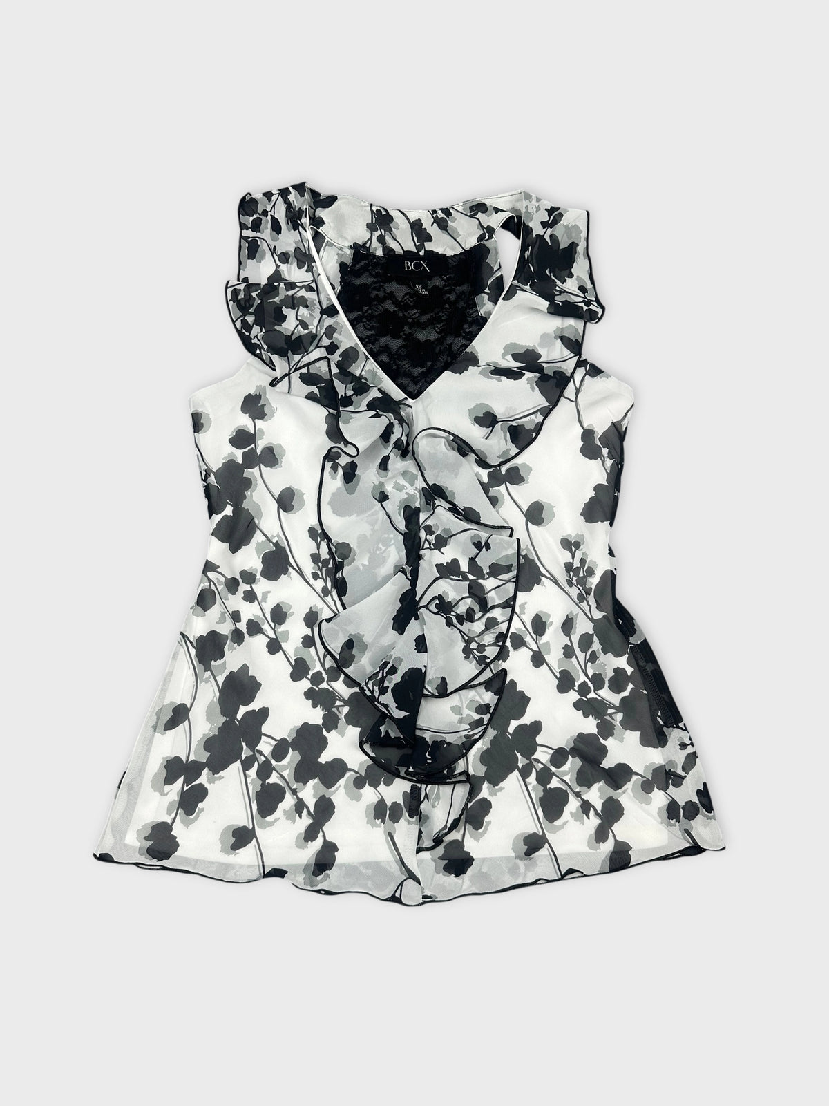 Front view of a sleeveless black and white floral top with ruffled trim.