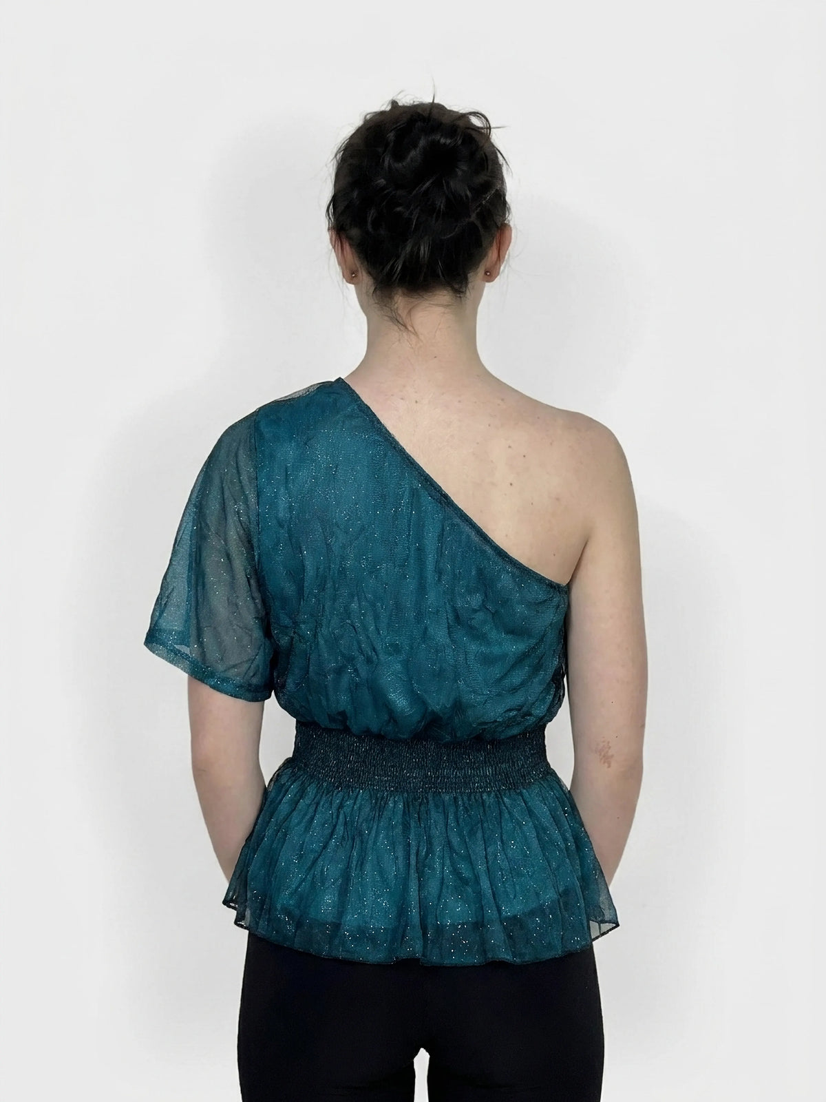 Back view of teal one-shoulder top featuring smocked waistband and sheer fabric.