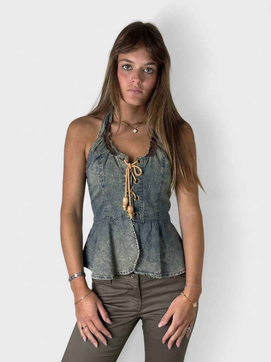 Front view of a denim peplum top with laces and a ruffled neckline.