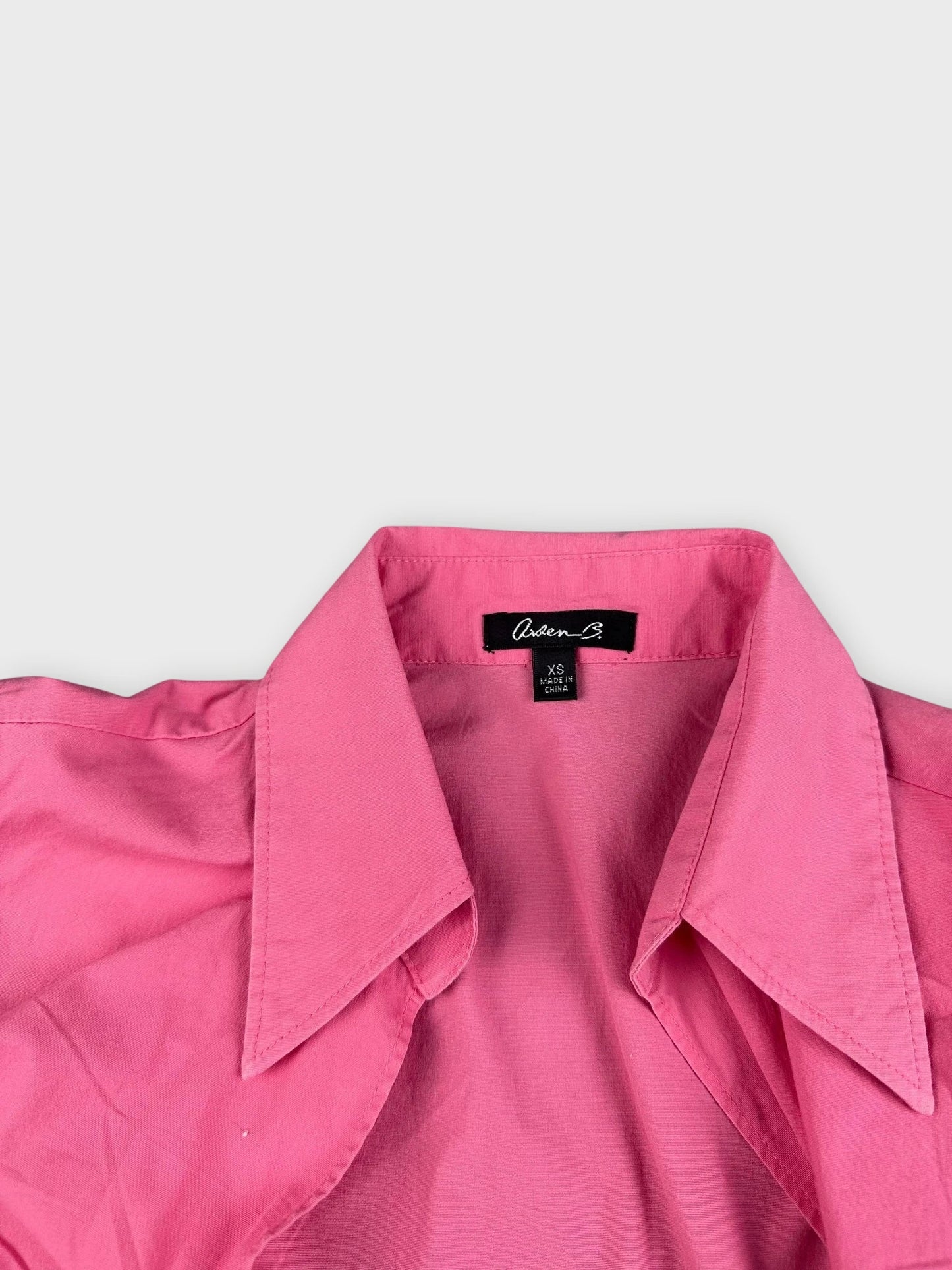 Detail view of a pink sleeveless button-down shirt with large collar.