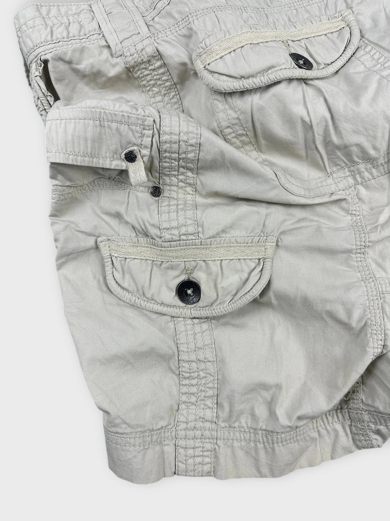 Beige mini skirt detail view showing side pockets and button closure design.