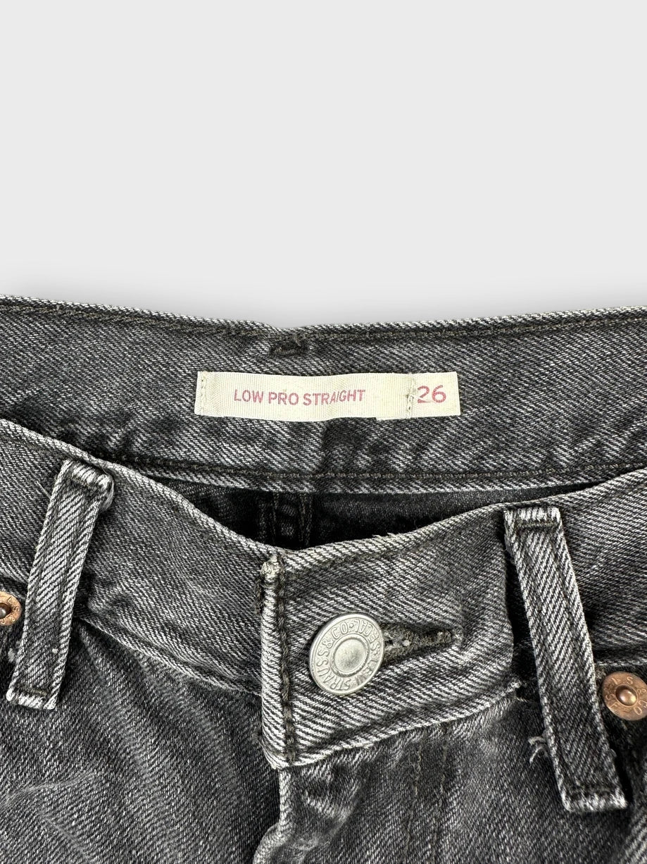 Detail view of black denim mini shorts featuring a distressed hem and button fastener.