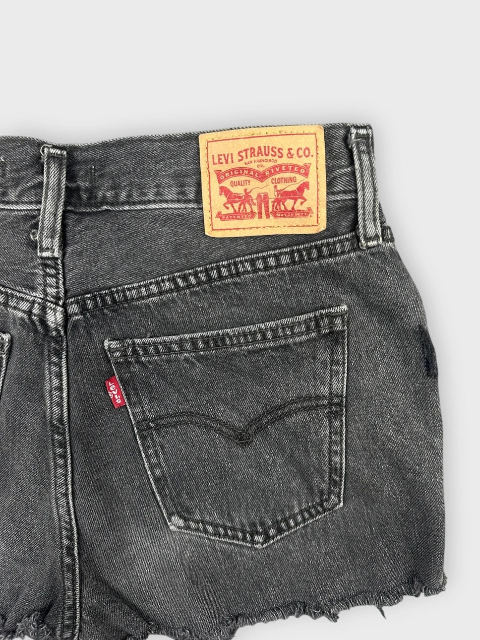 Detail view of black denim mini shorts featuring distressed hem and Levi's tag.
