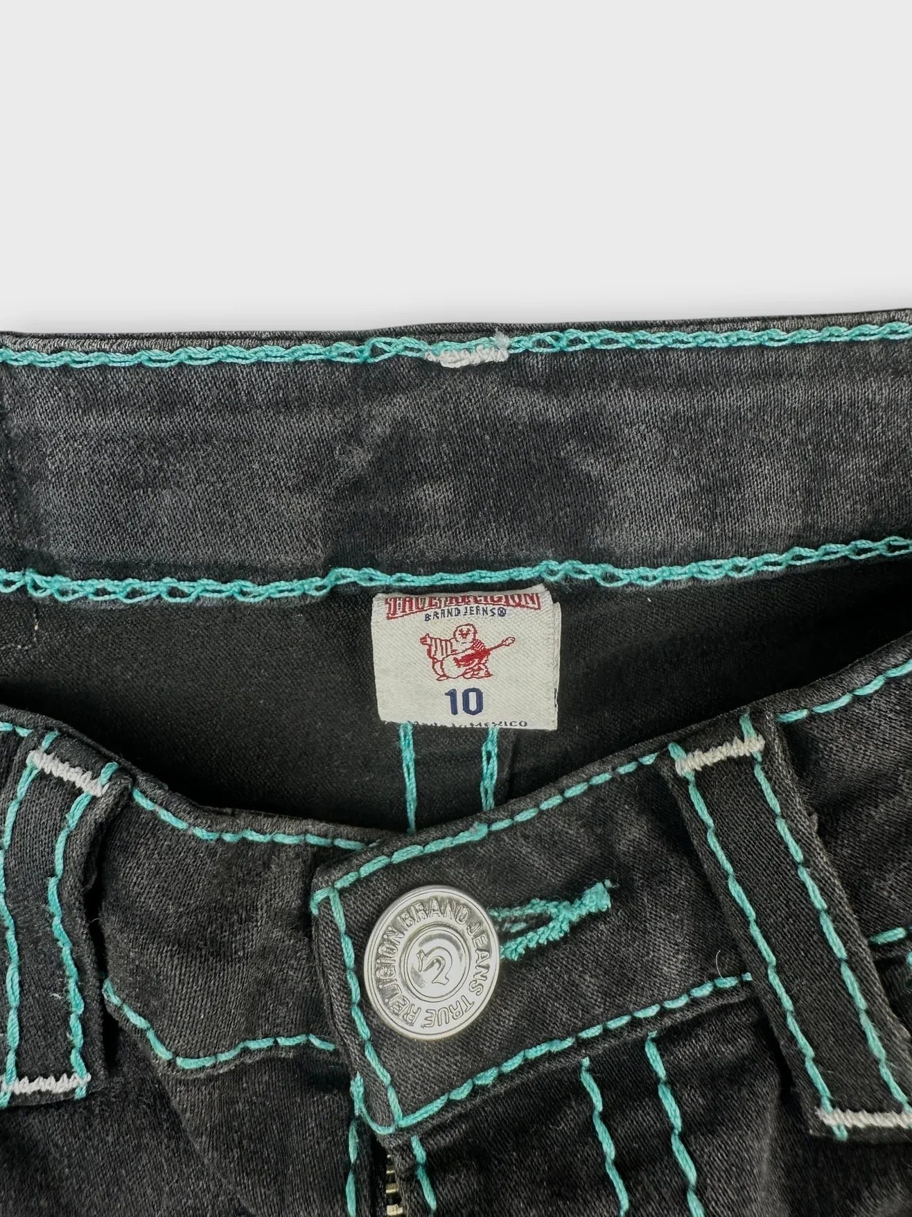 Detail view of black denim shorts with turquoise stitching and button closure.