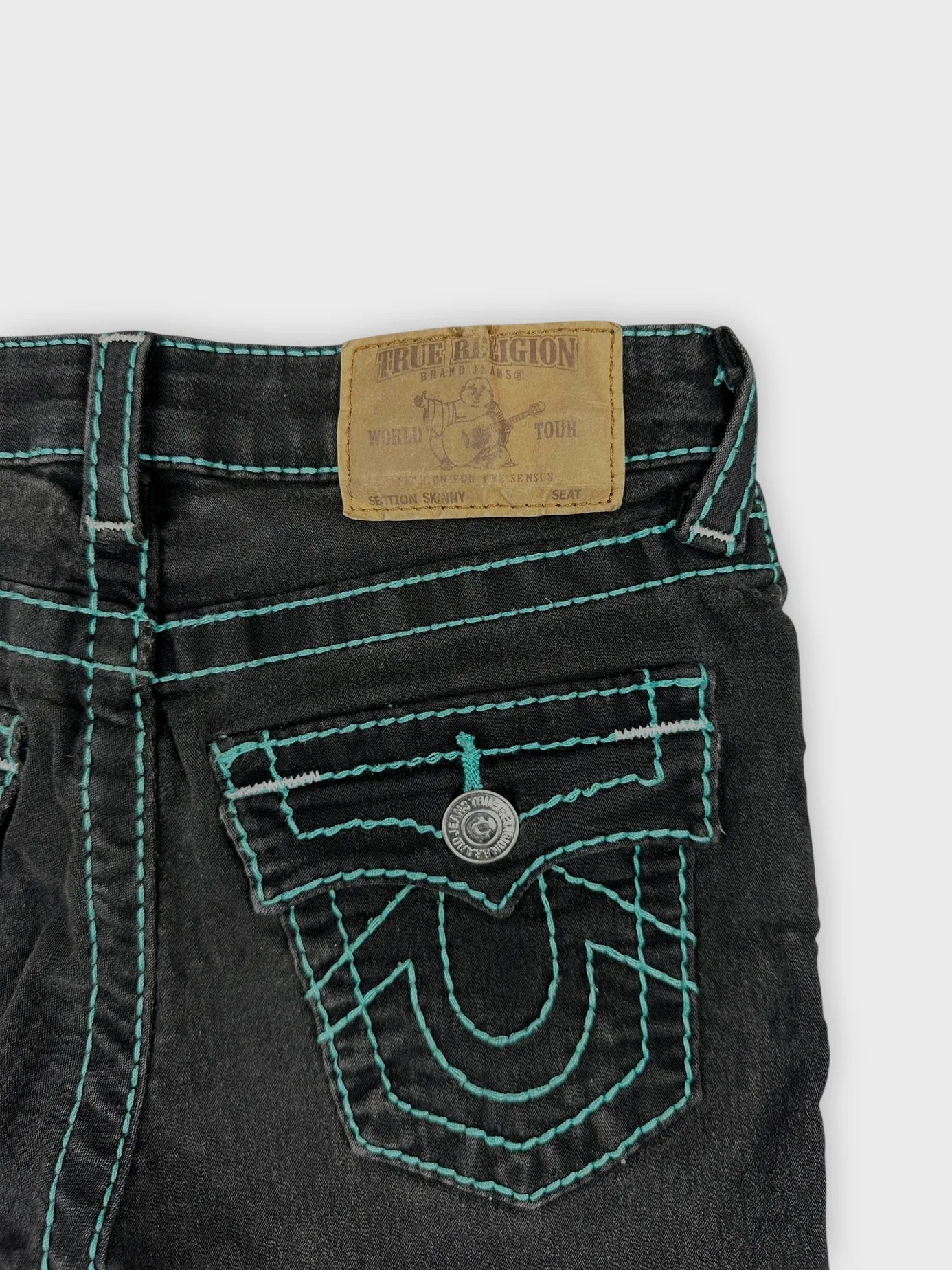 Detail view of black denim shorts featuring turquoise contrast stitching.