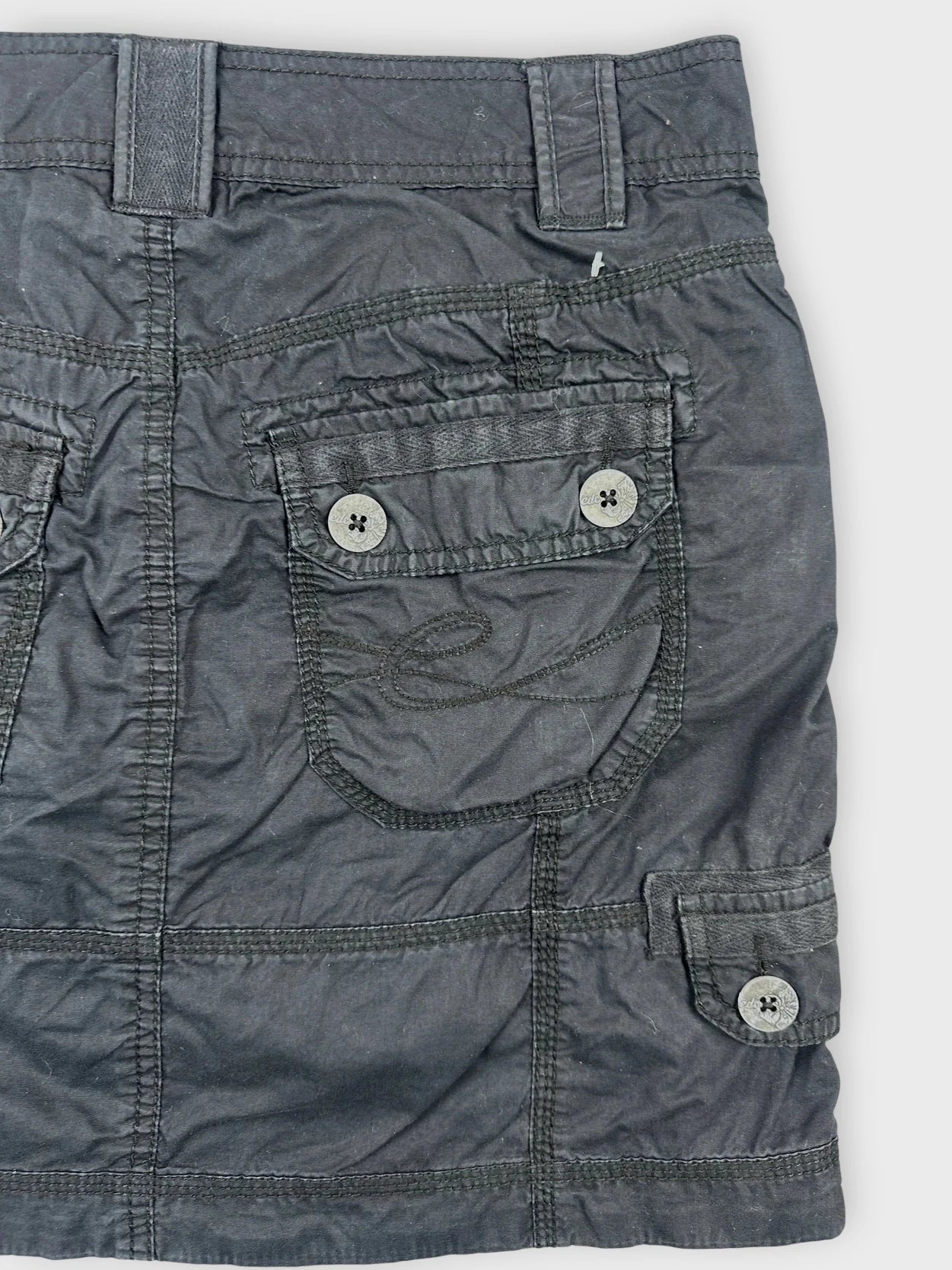 Black mini skirt detail view showing utility pockets and button closures.