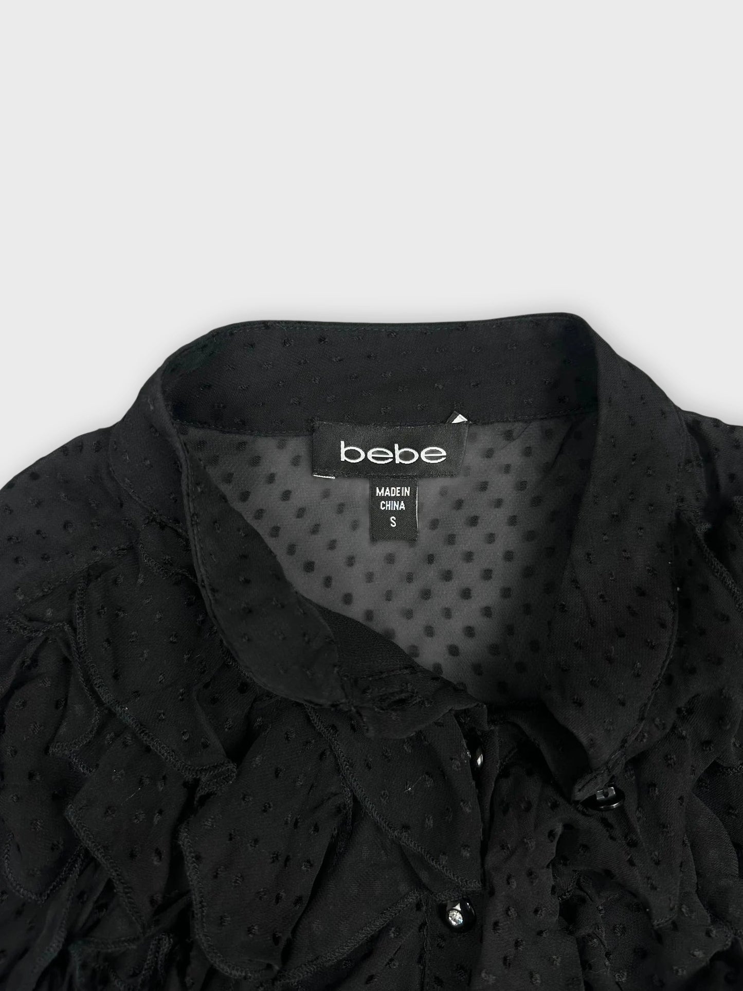 Detail view of a black ruffled blouse featuring button details.