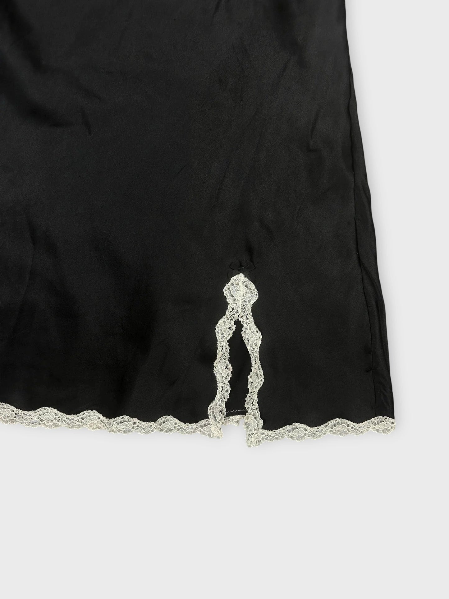 Detail view of black satin cami featuring white lace trim at the hem.