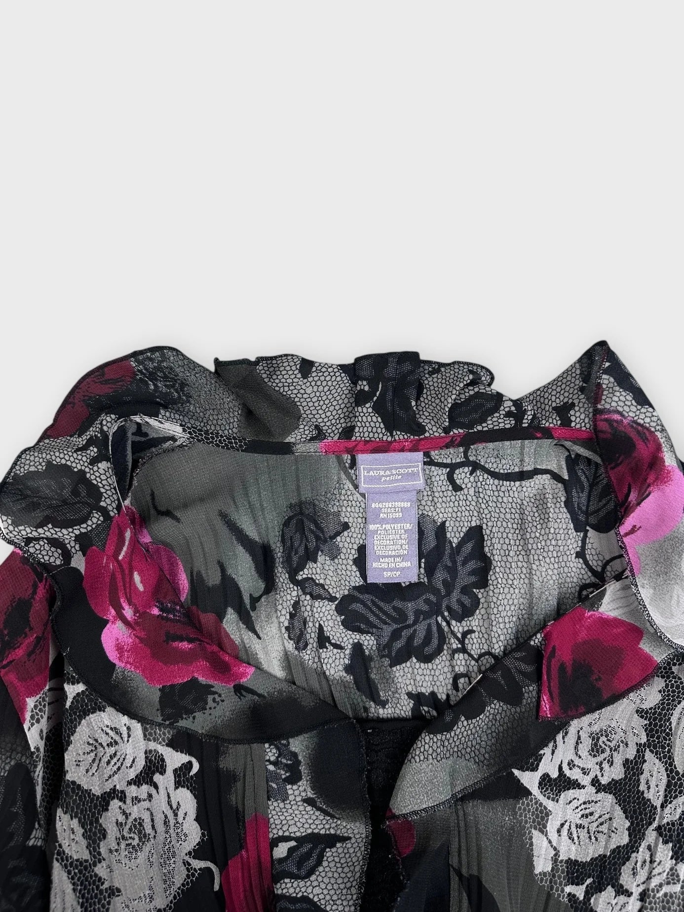 Detail view of a black floral blouse with pink accents and ruffled neckline.