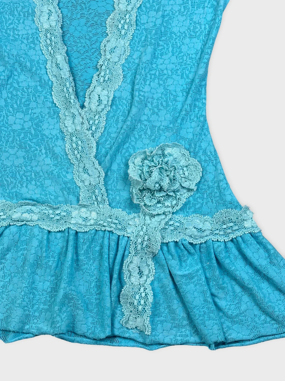 Detail view of a blue top featuring lace trim and a floral embellishment.