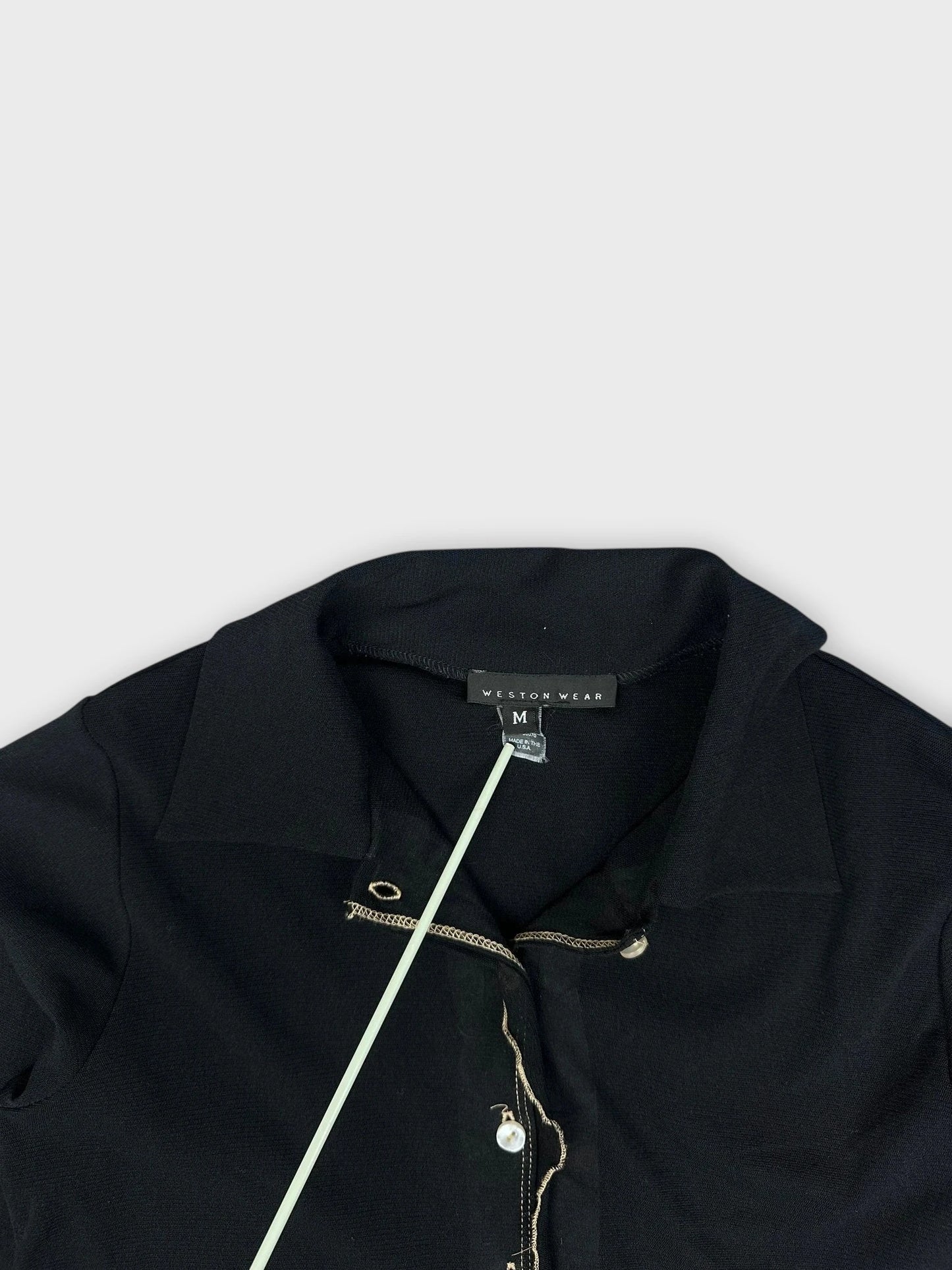 Detail view of a black collared shirt featuring a ruffled hem and pearl buttons.