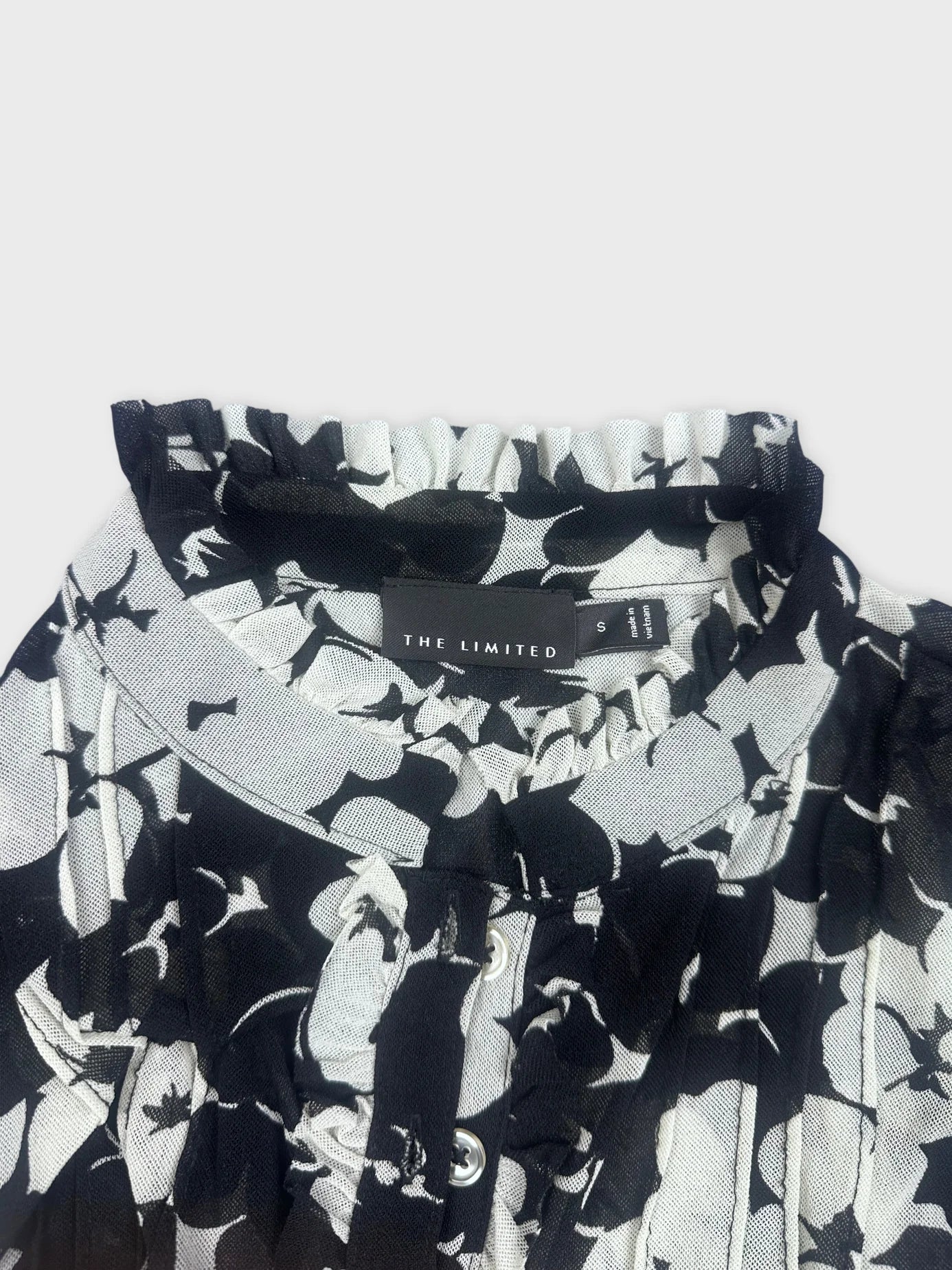 Detail view of black floral playsuit featuring ruffle trim and button closure.