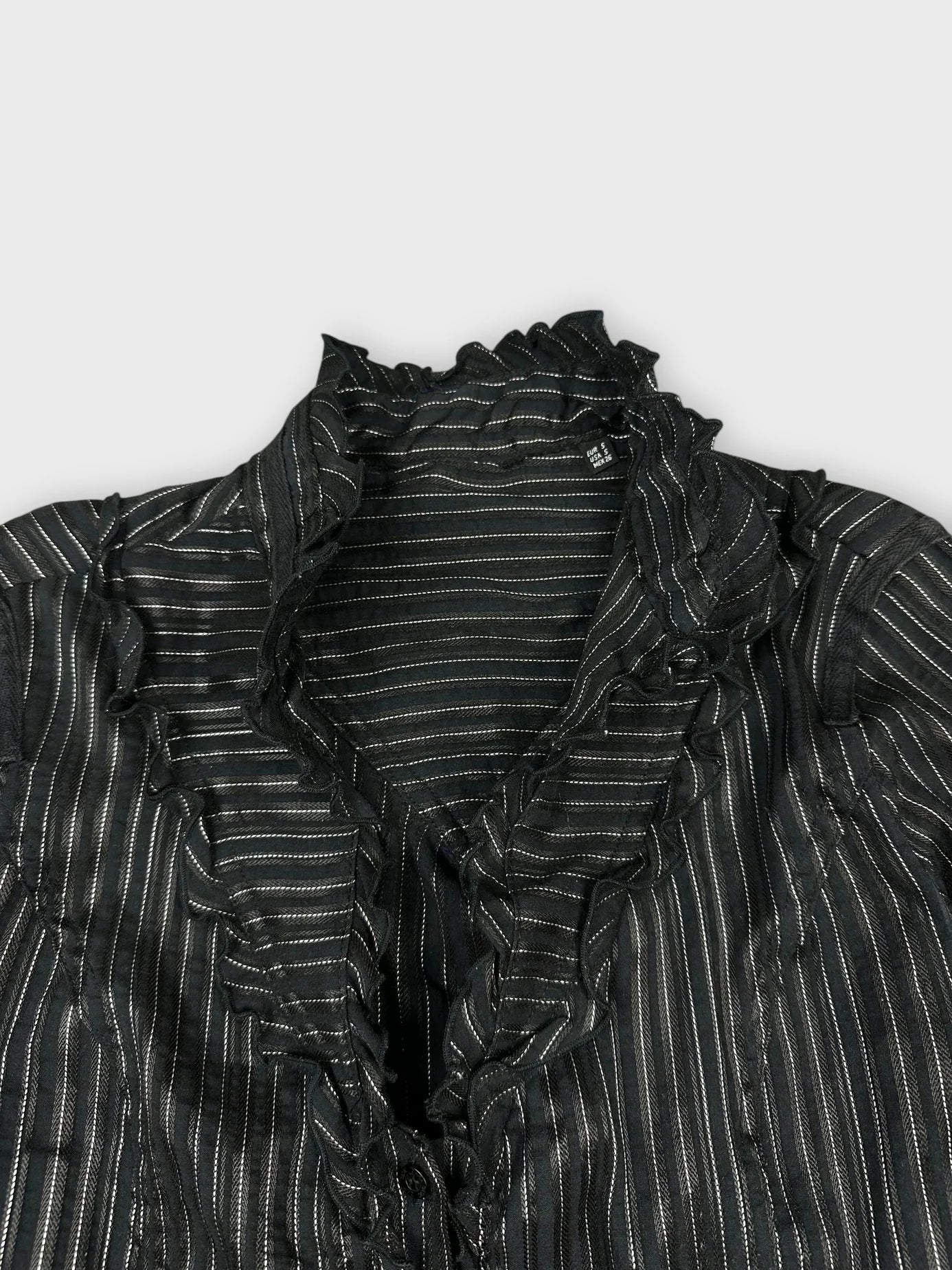 Detail view of a black ruffled blouse with silver stripes.