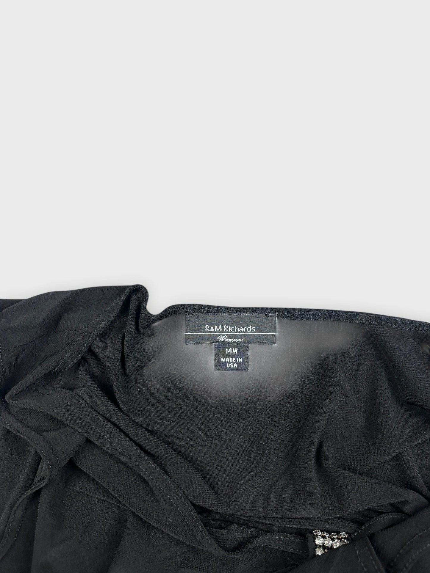 Detail view of a black top featuring a draped neckline and embellishments.