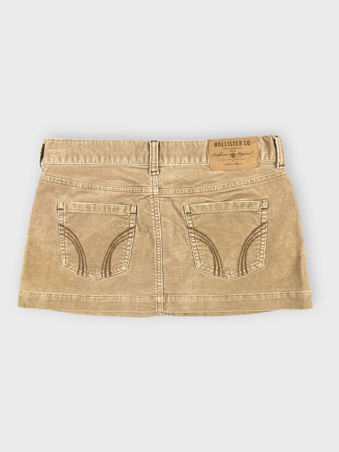 Back view of a brown denim mini skirt featuring stitched pocket details.