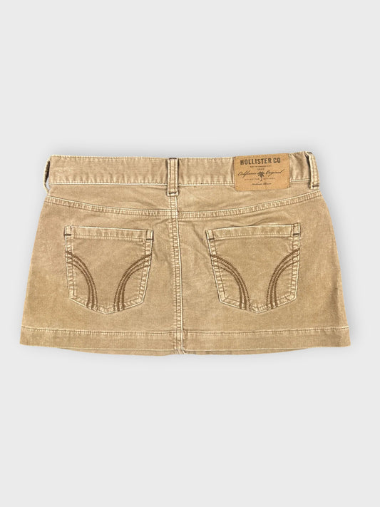 Back view of a brown denim mini skirt featuring stitched pocket details.