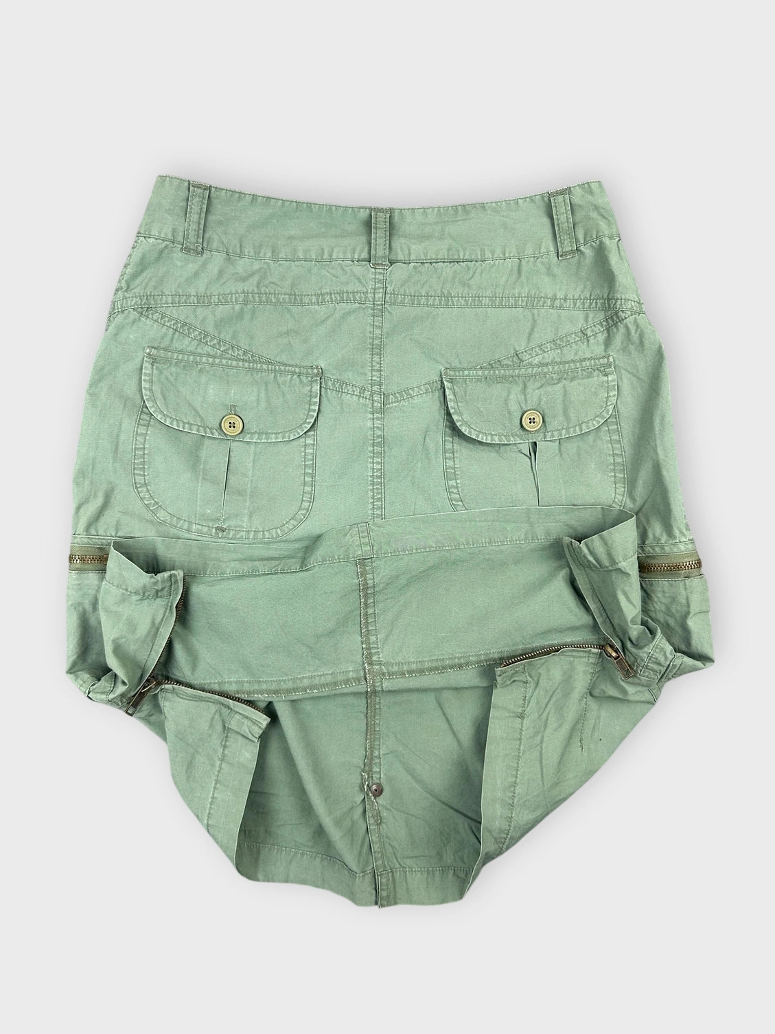 Detail view of a green mini skirt with zipper details and pockets