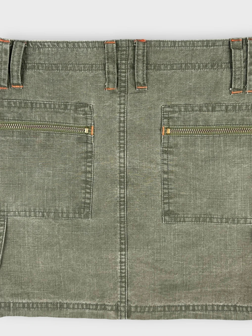 Detail view of olive mini skirt featuring side zippers and military-style pockets.
