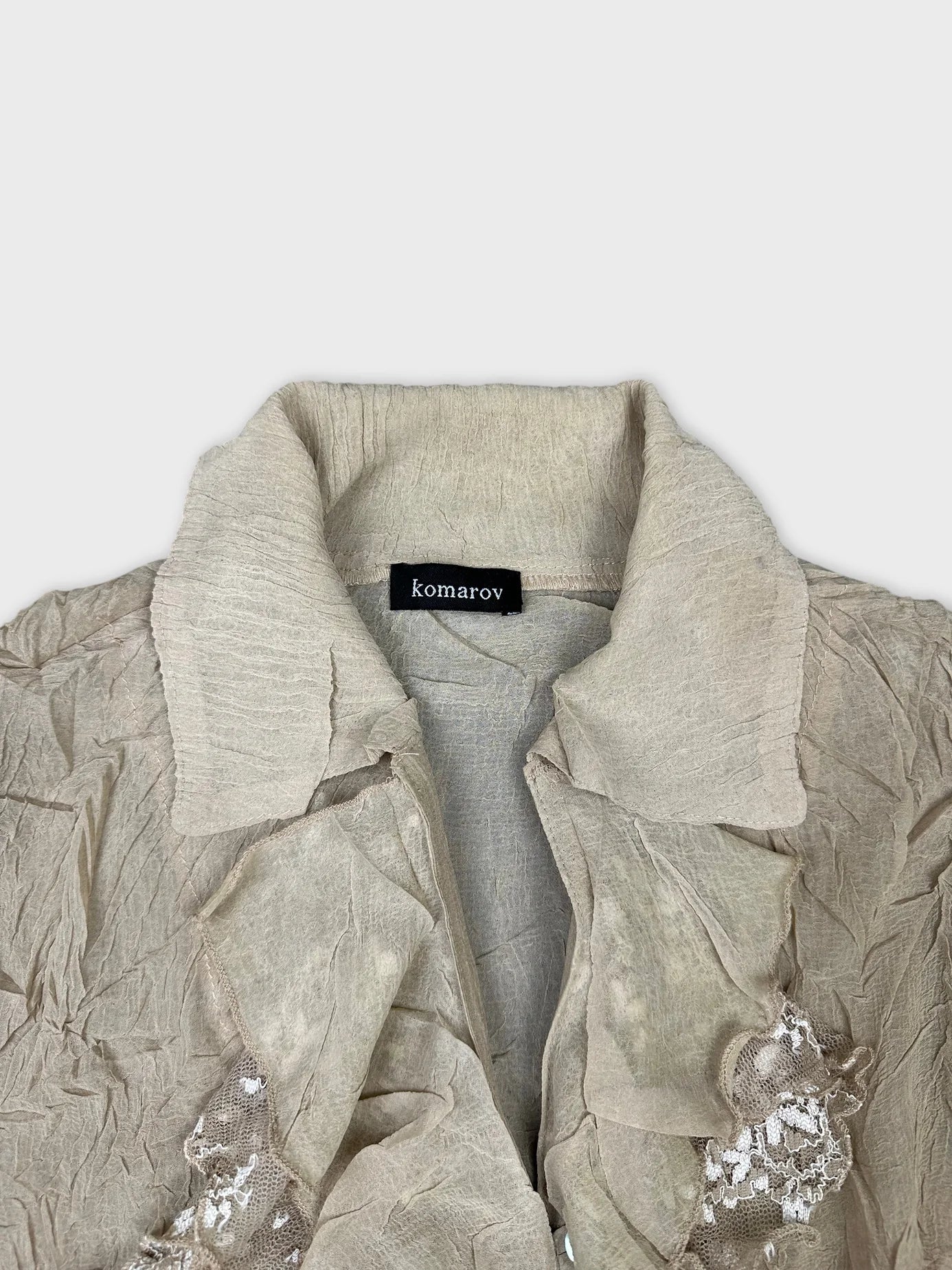 Detail view of a beige ruffled long sleeve top with lace trim.