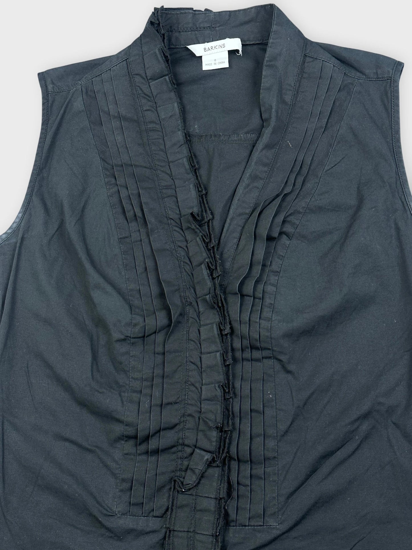 Detail view of a black sleeveless top featuring a ruffled front and pleats.
