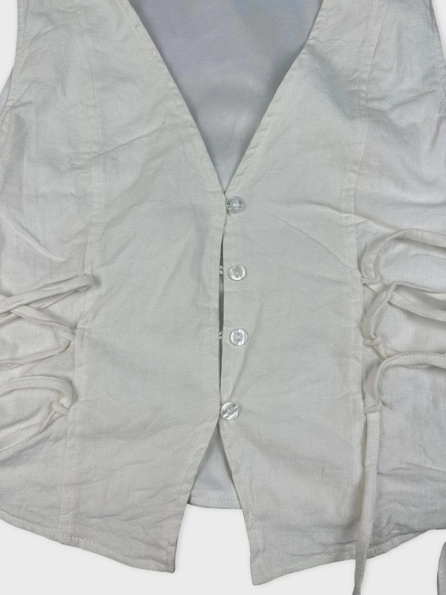 Detail view of a white lace-up linen top with side gathers.