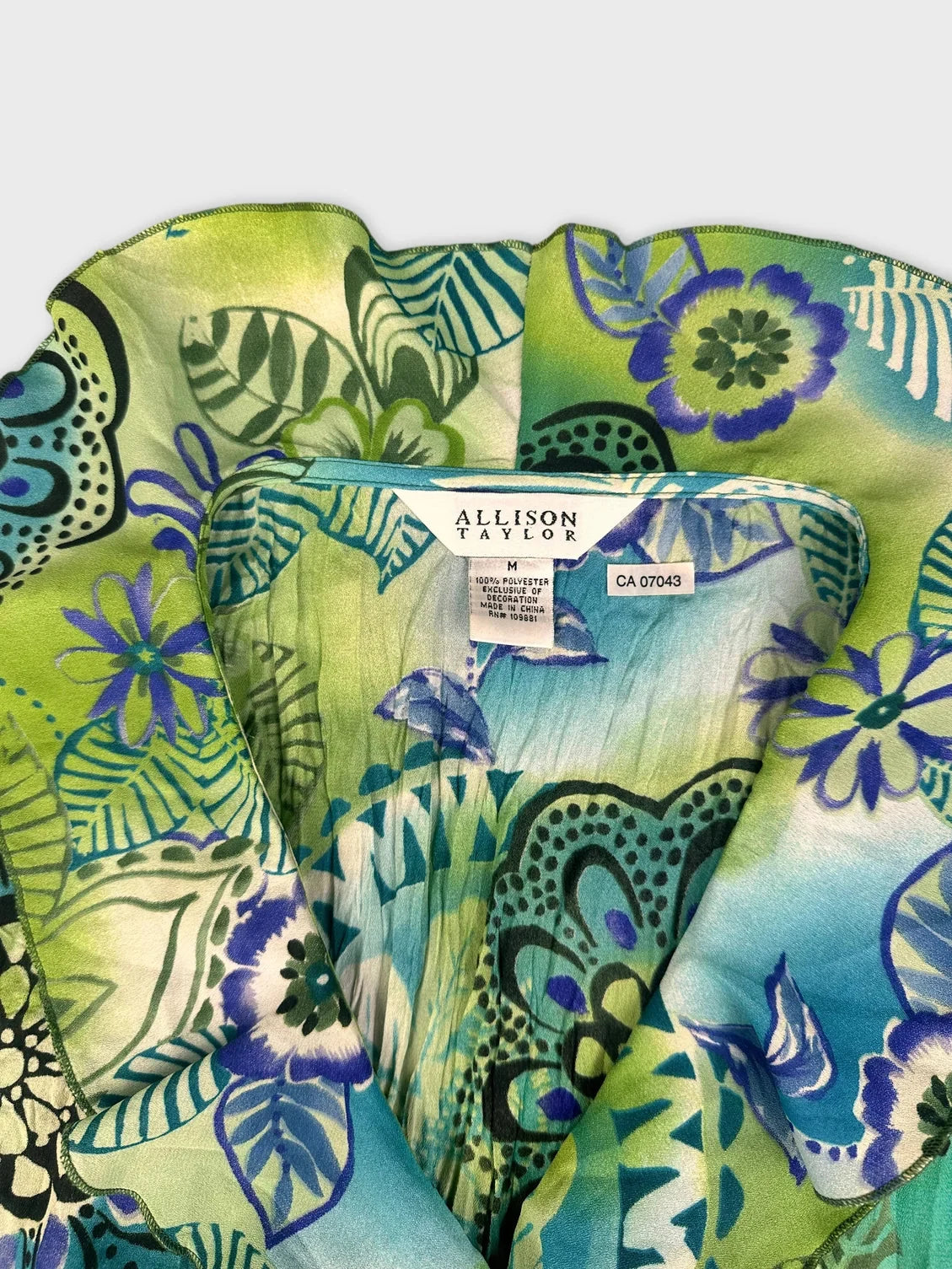 Detail view of colorful ruffle blouse featuring floral print in green and blue.