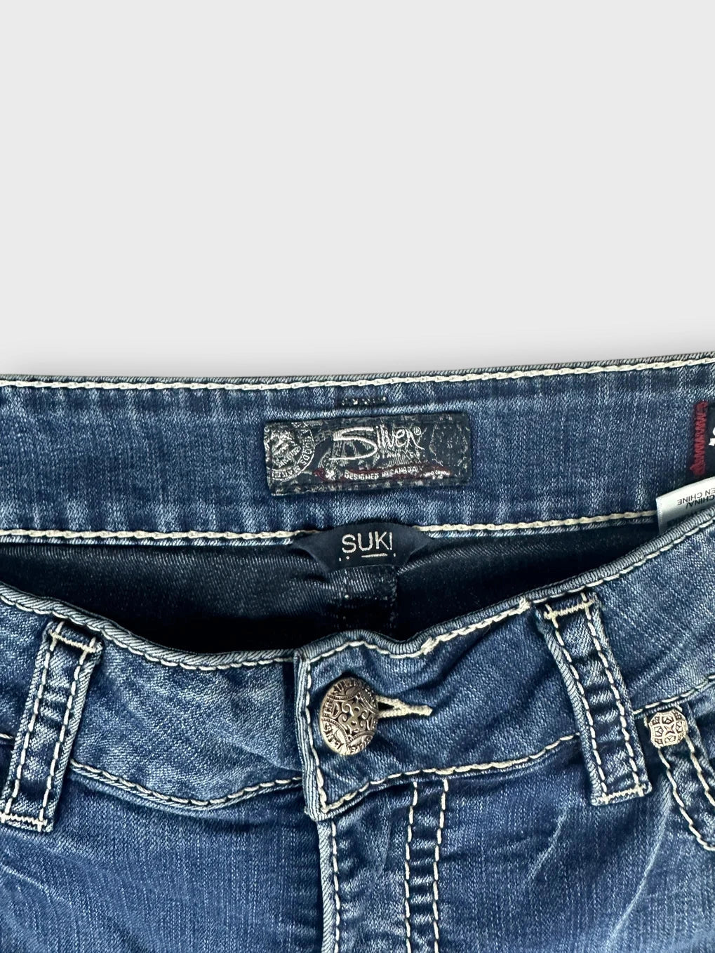 Detail view of blue denim jeans with a decorative button and stitch detailing.