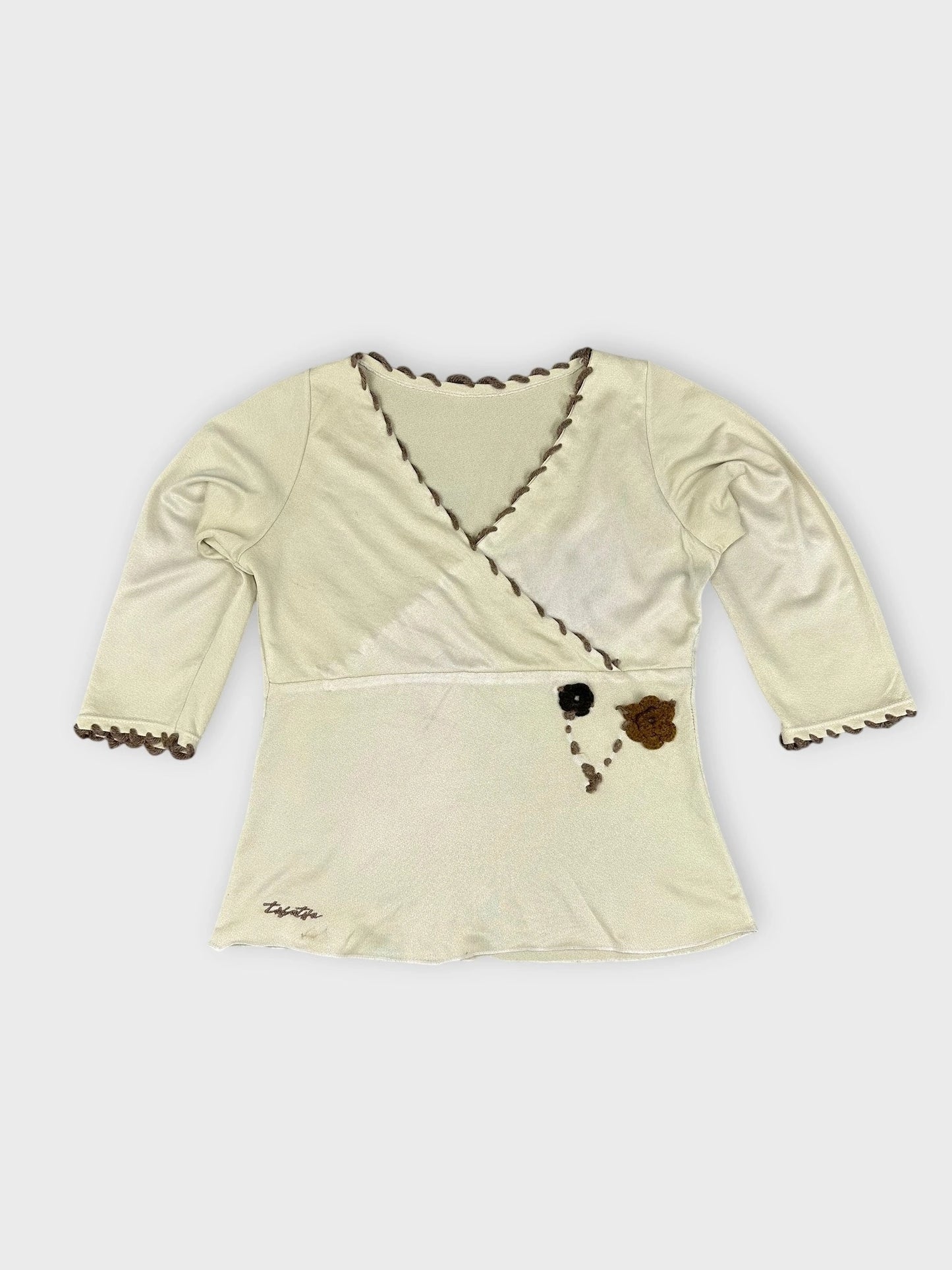 Detail view of a cream floral wrap top with scalloped edge trim.