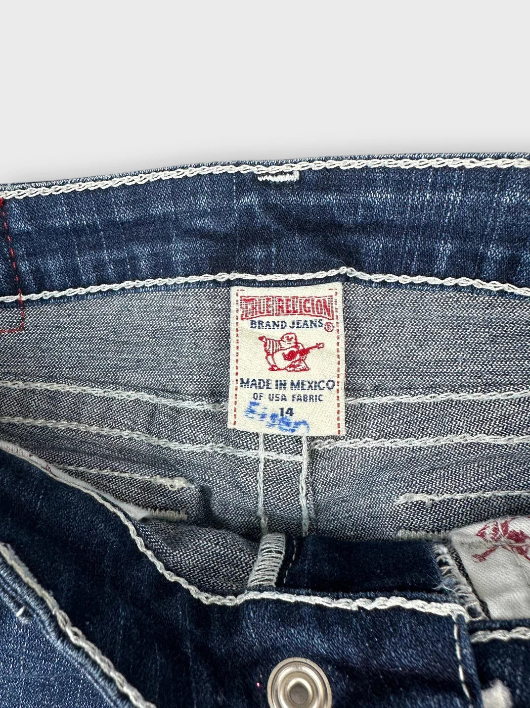 Detail view of dark denim cutoff shorts with red stitching.