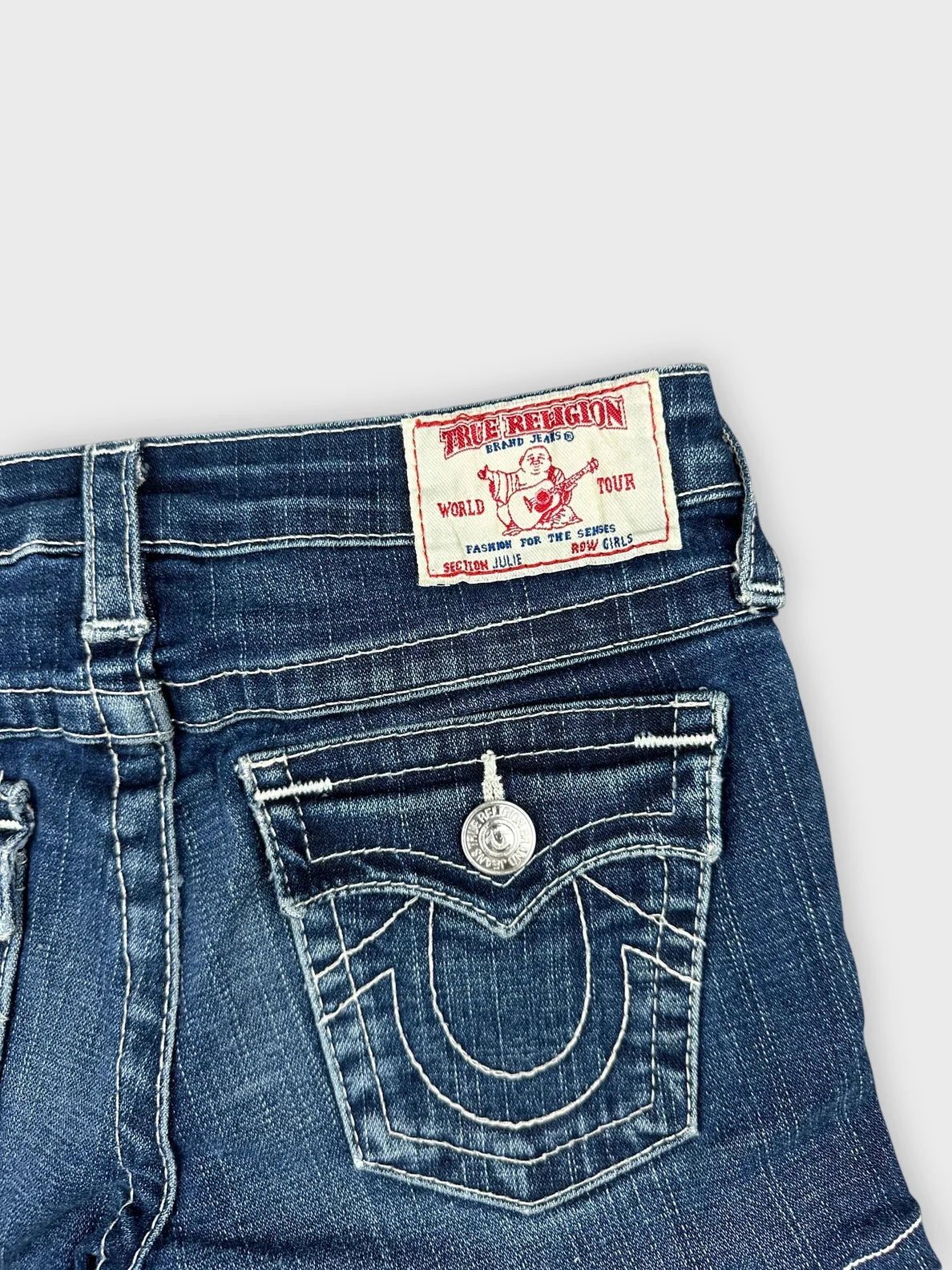 Detail view of dark denim cutoff shorts featuring edgy stitching and logo patch