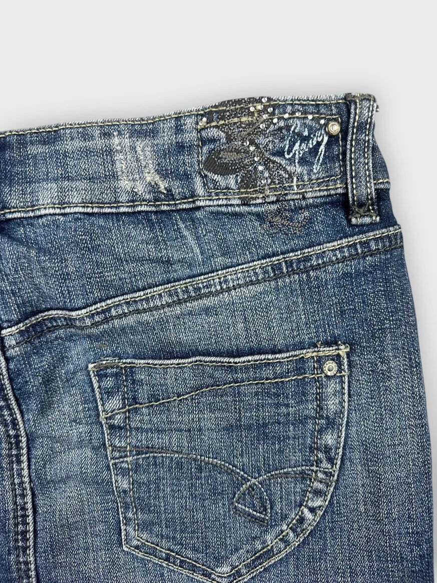 Detail view of a blue denim mini skirt with button detail and back pocket.