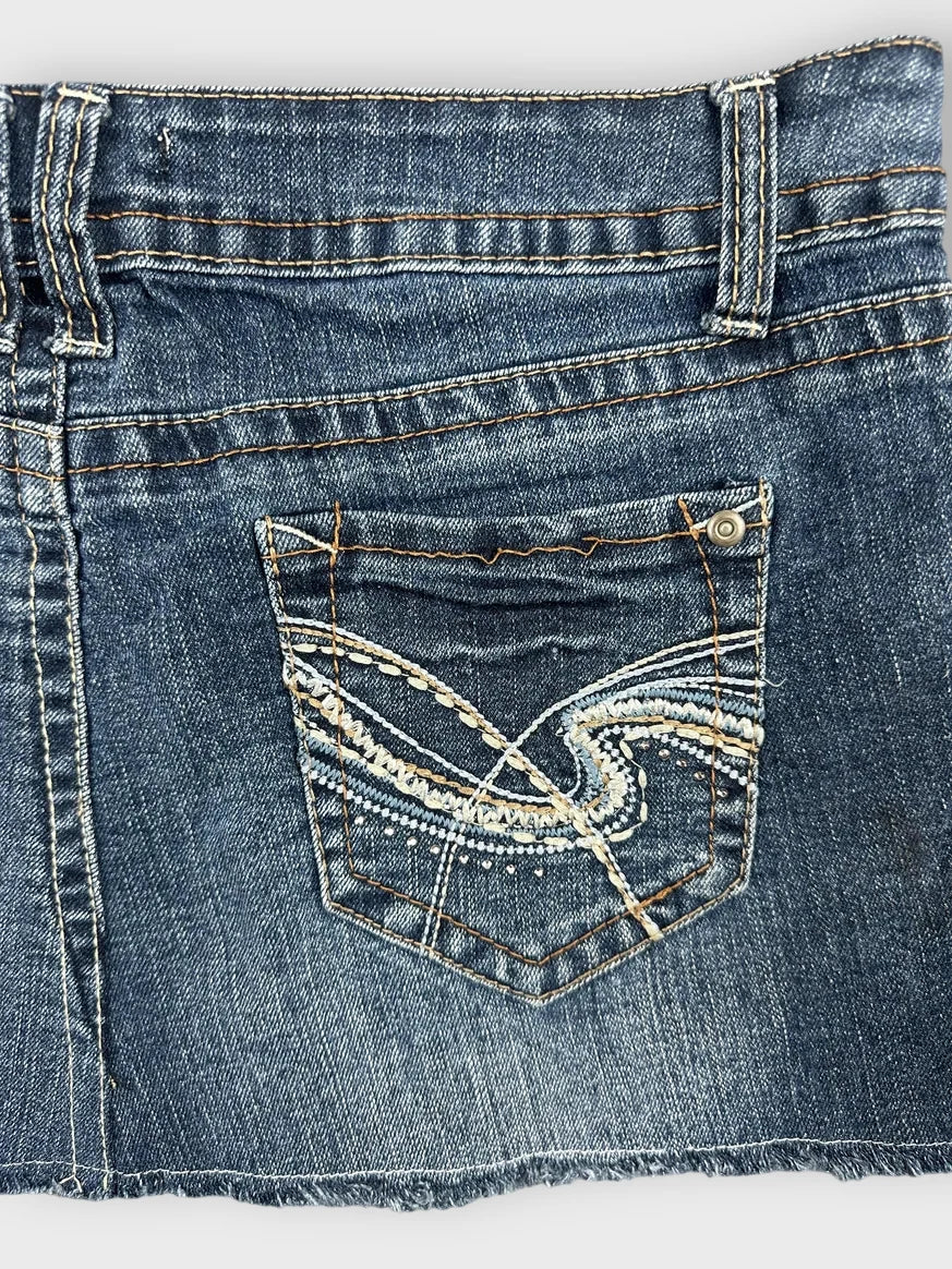 Detail view of a denim mini skirt in dark blue with embroidered pockets.