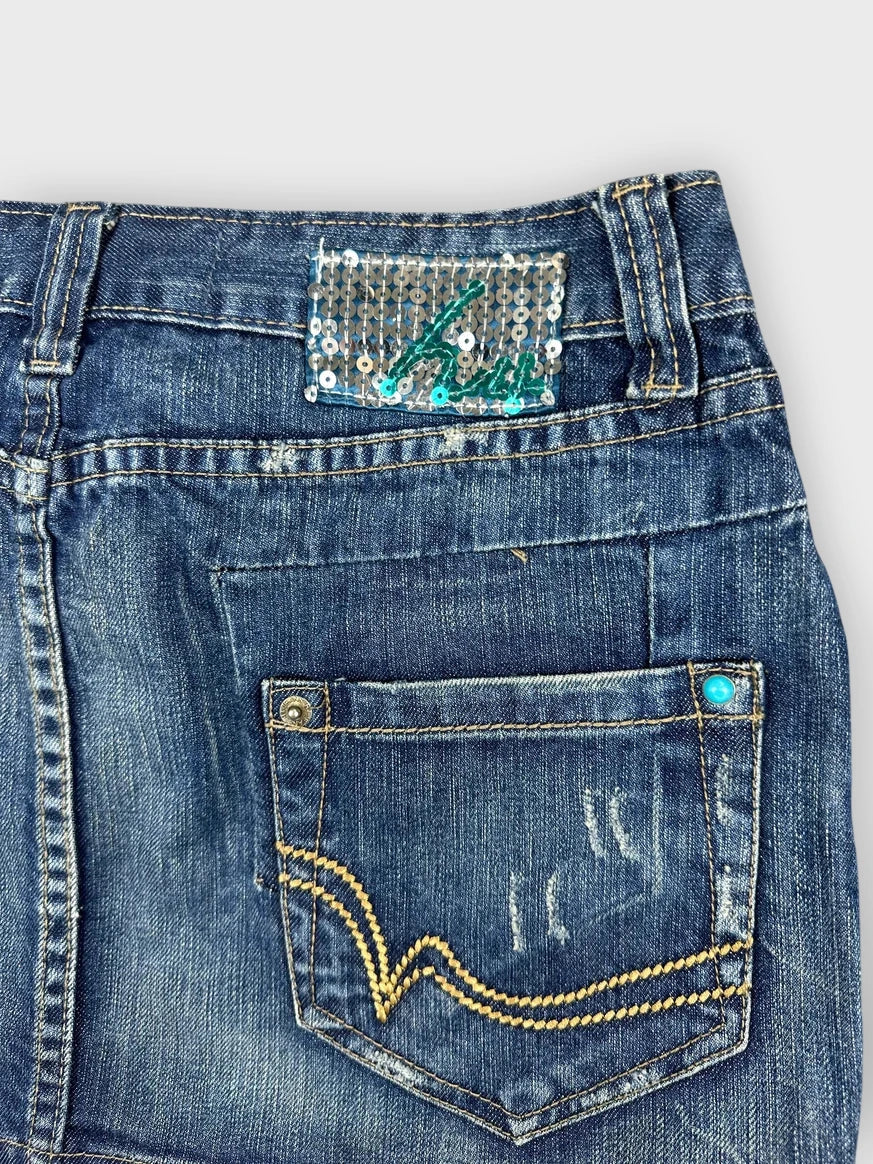 Detail view of a denim mini skirt showcasing a sequined label and back pocket.