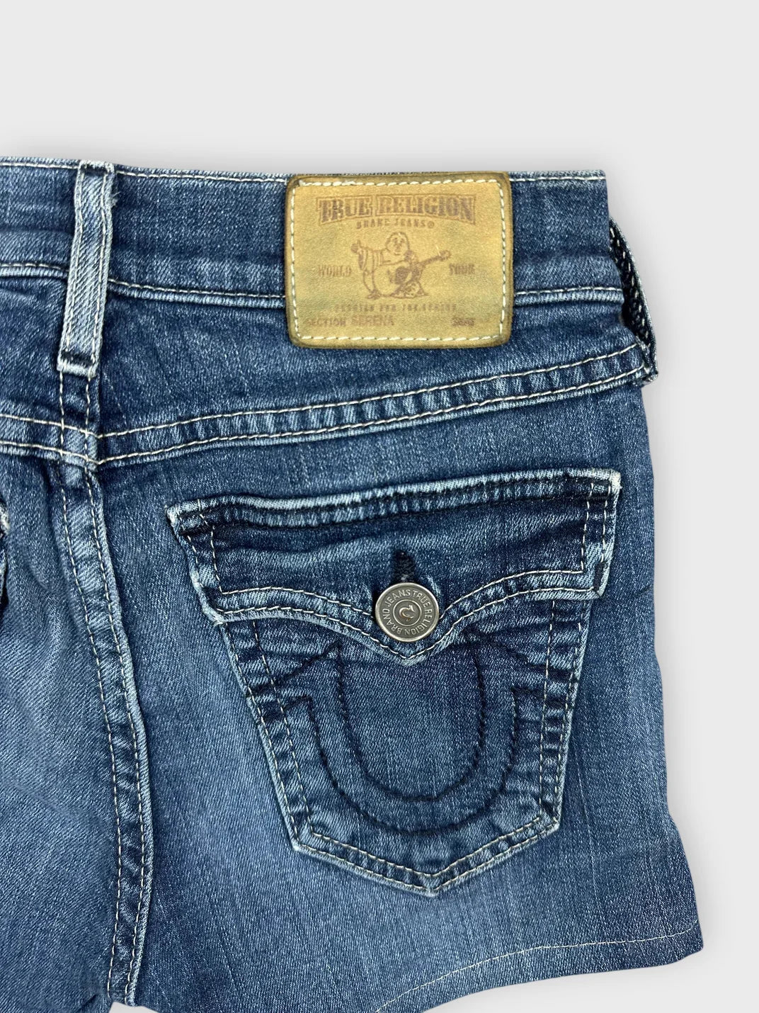 Detail view of denim shorts in blue with a frayed hem and logo tag.