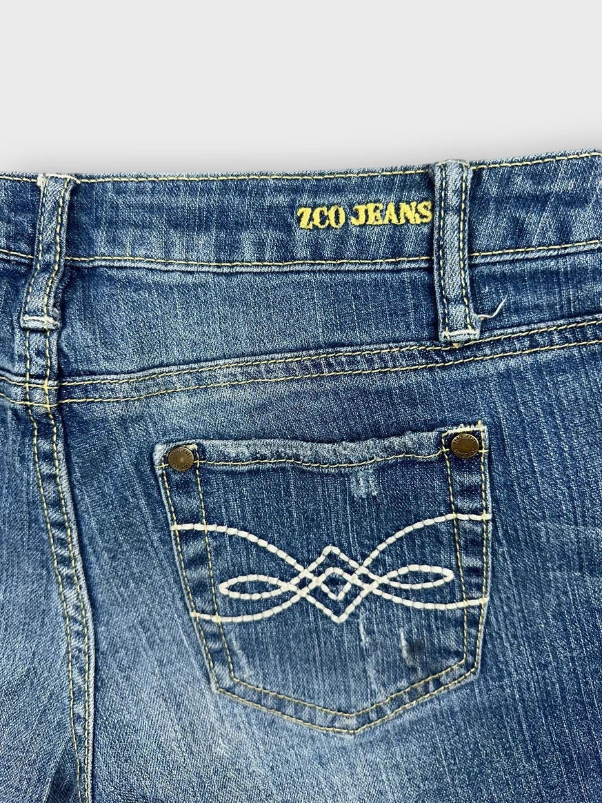 Detail view of distressed denim mini shorts in blue with decorative stitched pocket.