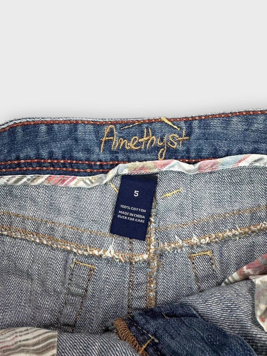 Detail view of distressed denim mini skirt featuring raw hem and blue fabric.