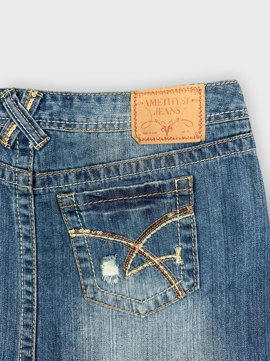 Detail view of a distressed denim mini skirt in blue with raw hem.