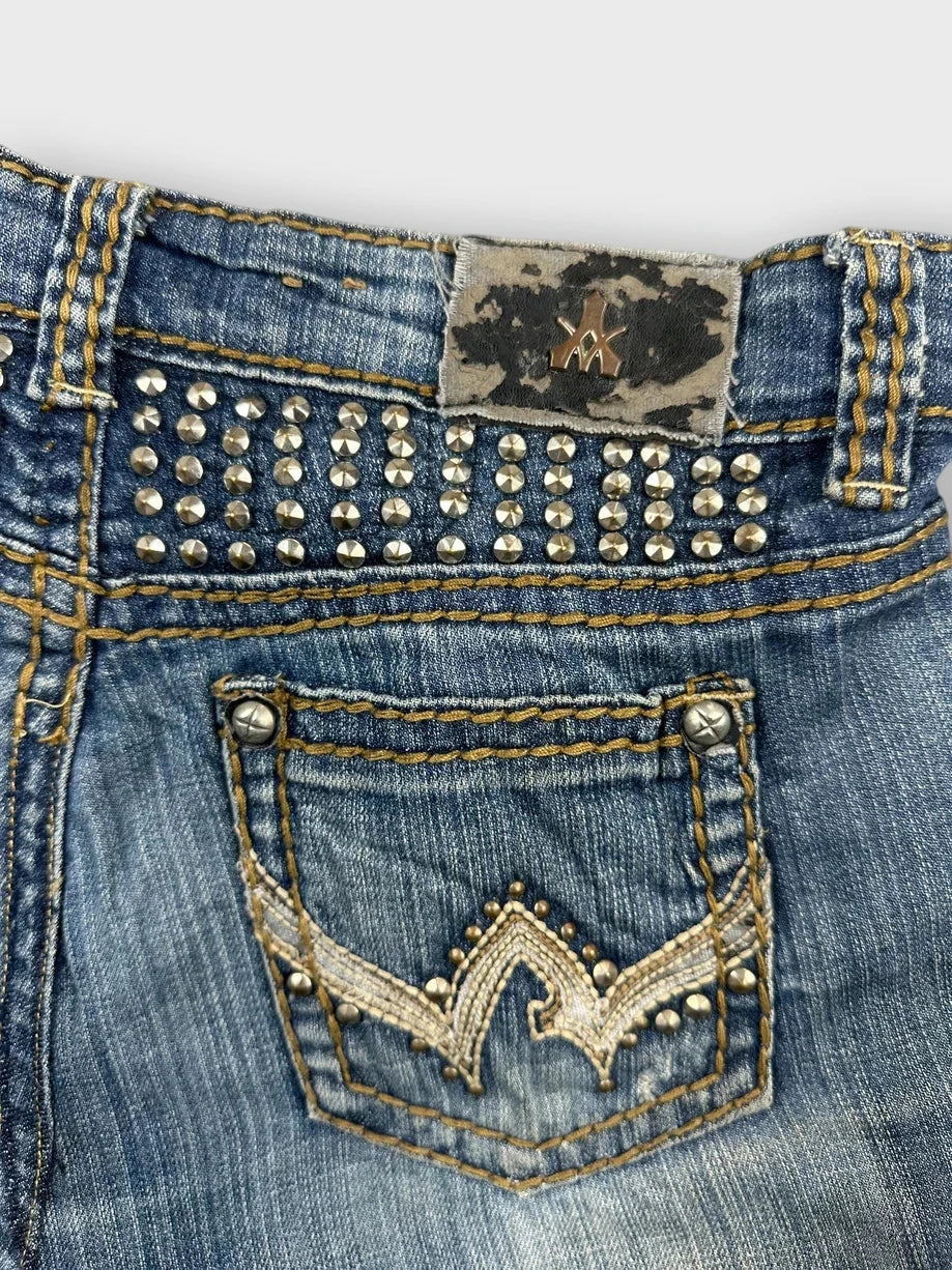 Detail view of a distressed denim mini skirt in blue with studded embellishments.