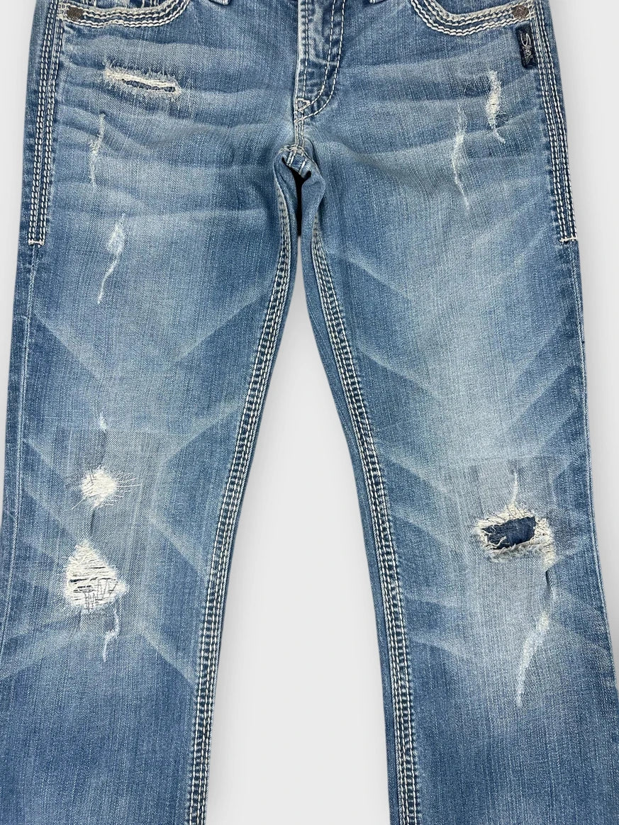 Detail view of distressed light blue denim jeans with worn-in patches.