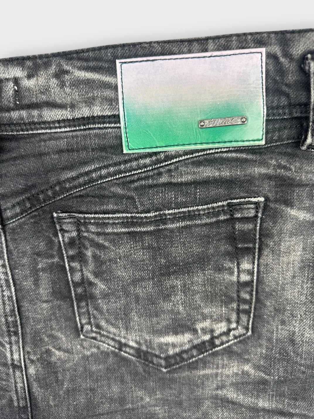 Detail view of black denim mini skirt showcasing back pocket and tag.