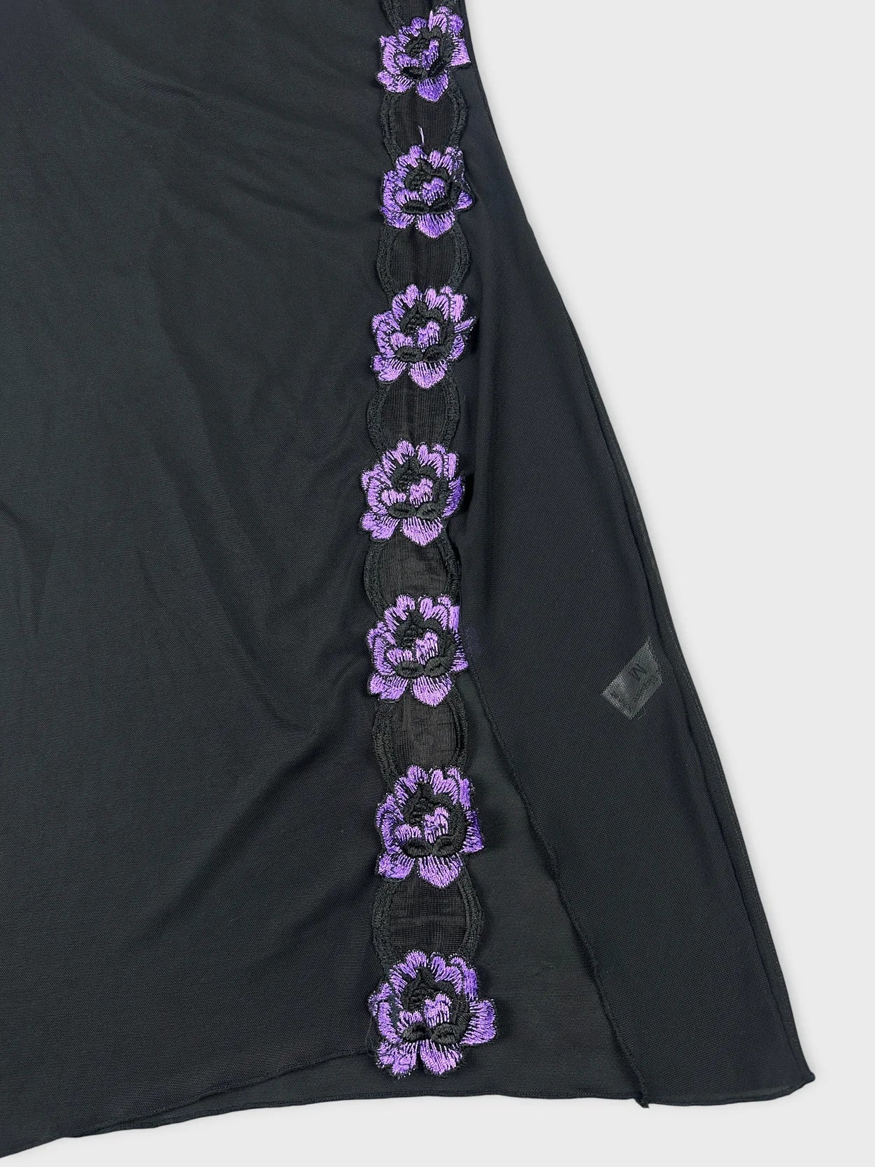 Detail view of black mesh tank top with purple floral embroidery.