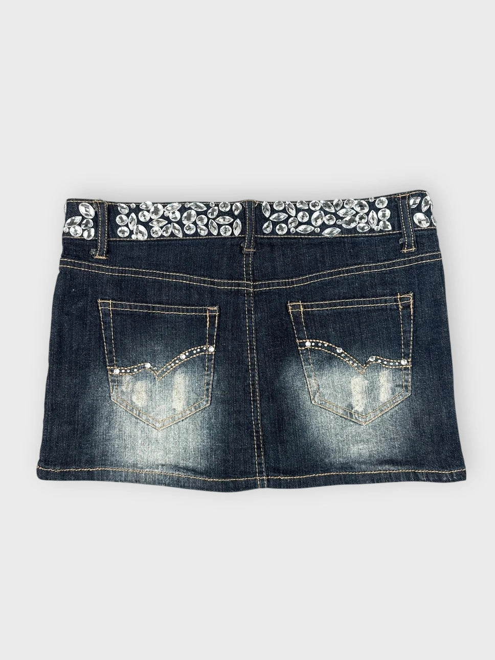 Detail view of a dark blue denim mini skirt with embellished waistband.
