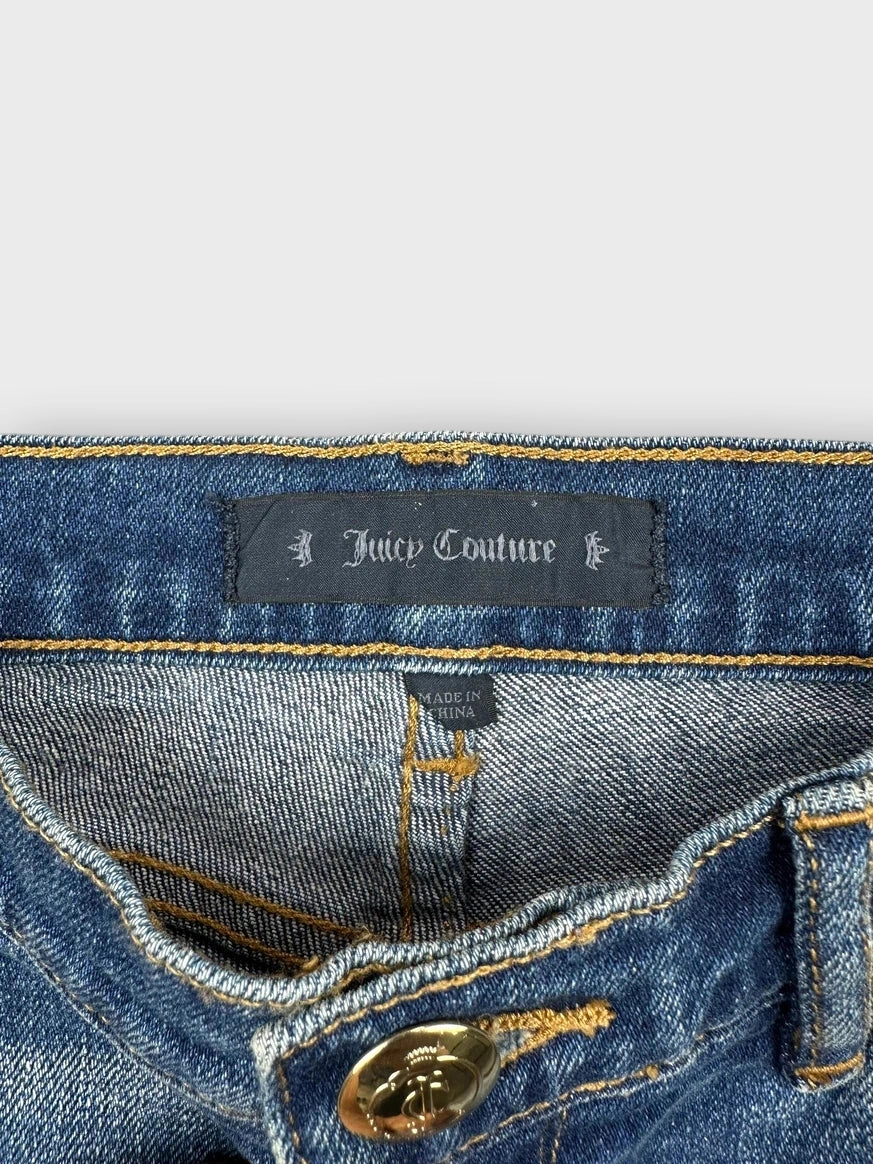 Detail view of blue denim mini shorts with gold button and black embroidery.