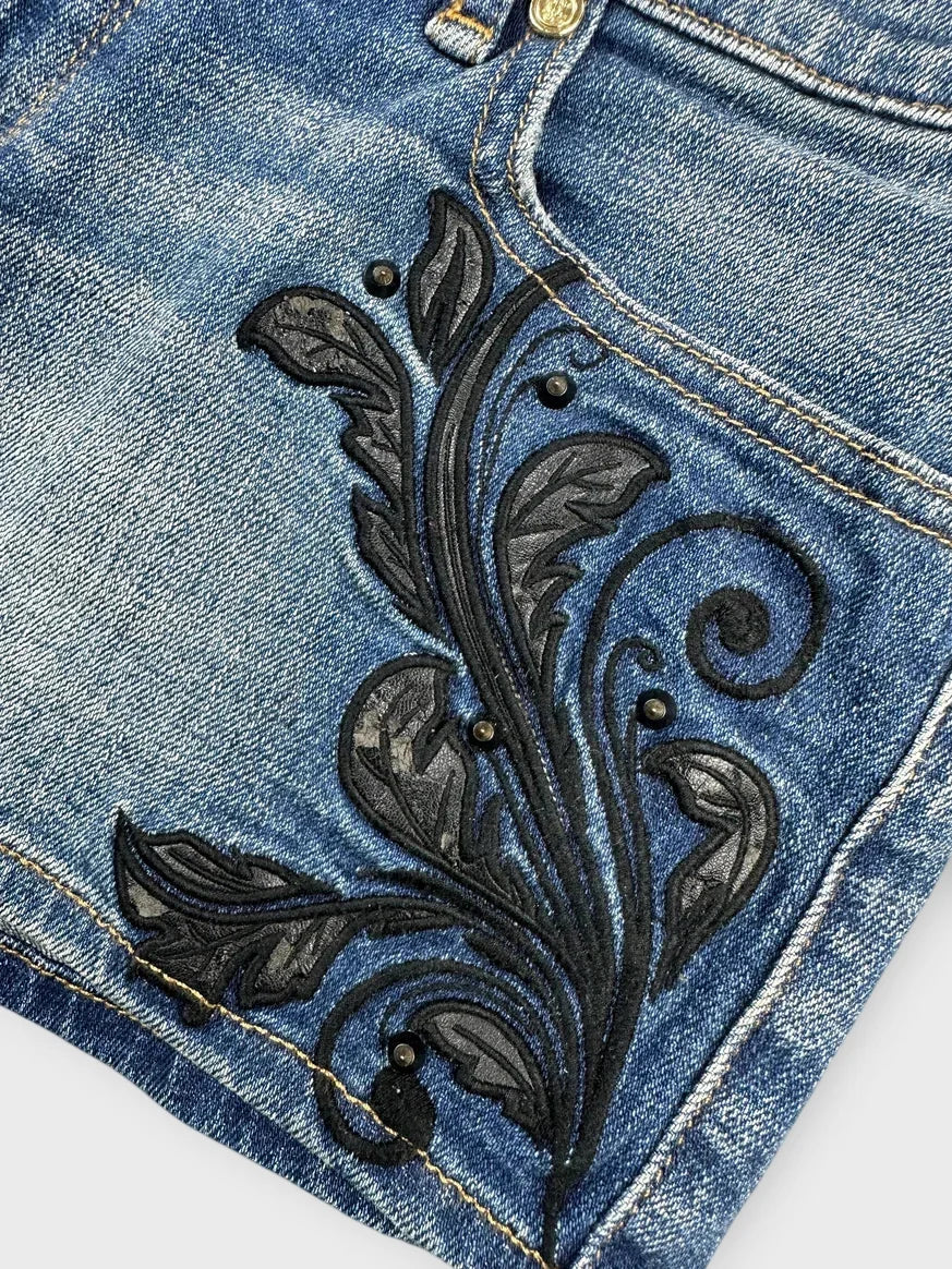 Detail view of light blue embroidered denim mini shorts with black floral pattern.
