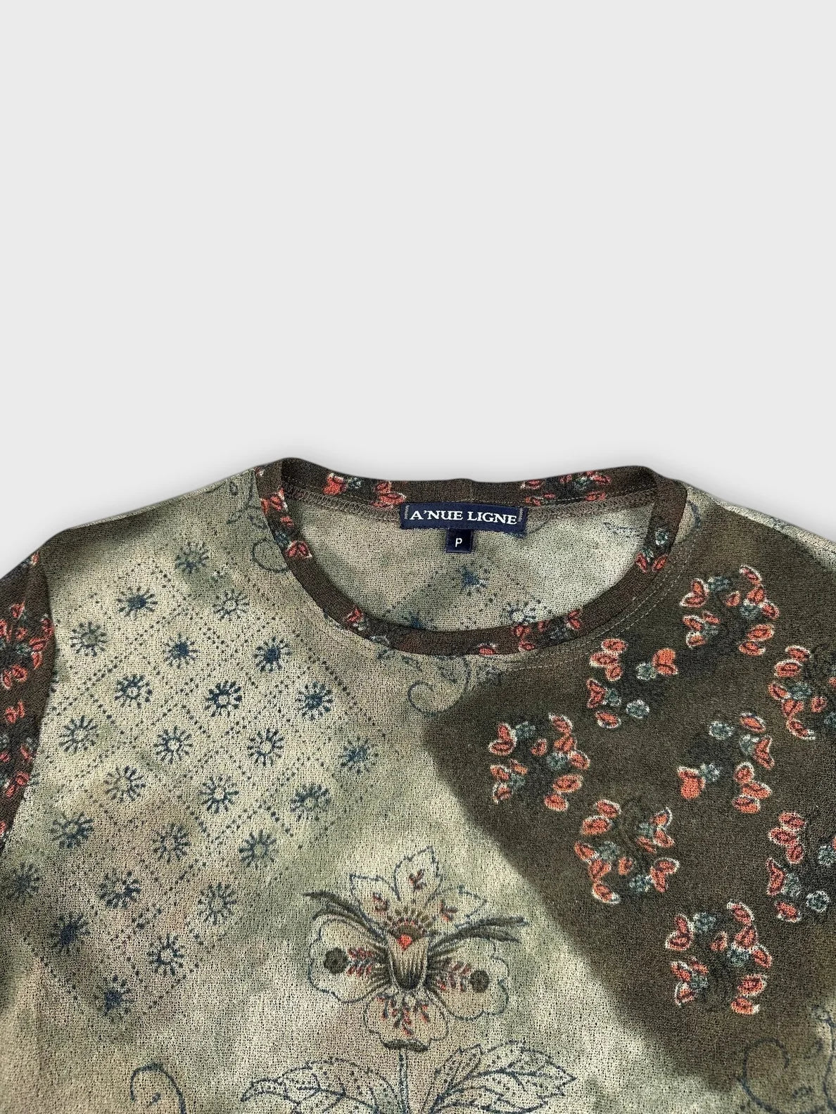 Detail view of a floral patchwork long sleeve top in soft green with intricate prints.